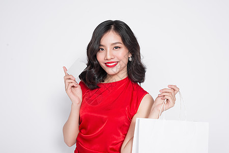 穿着红裙子的漂亮亚洲女人 带着购物袋 拿着信用卡站在白头黑脸上购物者配件礼物销售折扣中心情绪依赖购物店铺图片