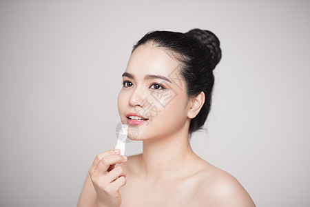 亚裔女性在灰色背景上施用卫生唇膏治疗化妆品香脂口红嘴唇白色唇部疱疹皮肤护理图片