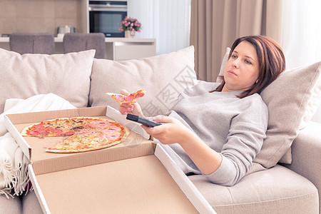 悲哀的女人吃披萨 拿着电话 在沙发上铺在家中 温暖的黄音图片