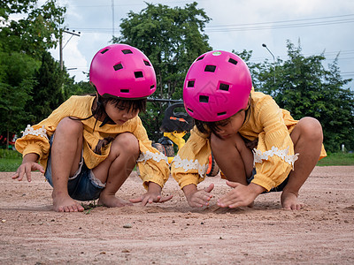 两个穿着头盔的可爱小姐妹 在阳光灿烂的夏天在公园里玩沙子 骑自行车后休息 发展想象力和探索 (笑声)图片