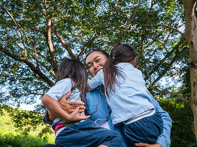 两个兄弟姐妹的小女孩和妈妈在温暖而阳光明媚的夏日在花园里互相欢笑和拥抱 年轻的女孩和她的母亲在公园里度过一天娱乐闲暇姐姐家庭女性图片