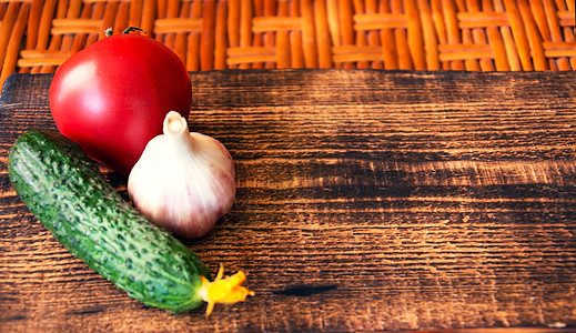 绿黄瓜 红番茄和大蒜躺在木板上的木制切割板上 其背景是用木制的桌子图片
