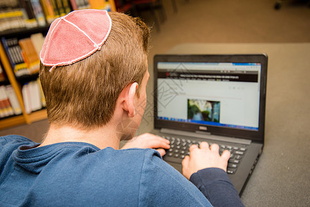 身穿Yarmulke背部的犹太男孩坐在教室里 与学生一起上课架子后脑勺年轻人男性女士笔记本电脑图书馆骷髅学校图片