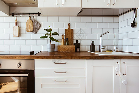 厨房黄铜器具 厨师配件 有白色瓦片墙壁和木桌面的垂悬的厨房 厨房背景的绿色植物财产公寓烤箱家具瓷砖住宅桌子器具植物木头图片