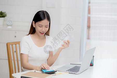 年轻的亚洲女性在家里用桌上的计算器计算财务家庭 女孩检查账单并成功节省家庭开支 债务清偿 税务和会计 商业概念微笑支付帐户写作电图片