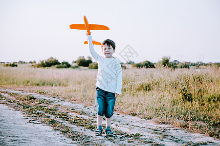 一个男孩在夏天在大自然中的飞机上玩耍 男孩梦想着未来 购买房地产广告 一篇关于选择职业的文章 一个快乐的孩子蓝色玩具活动空气飞行图片