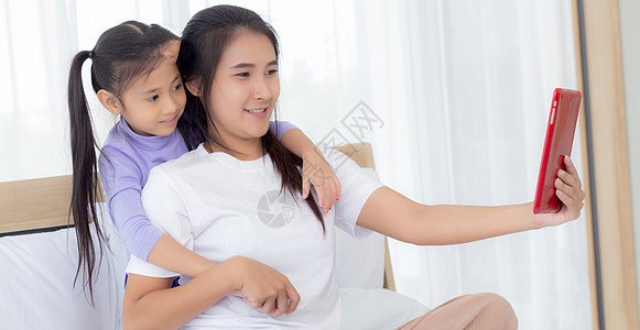 年轻的亚洲妈妈和女儿在平板电脑上视频通话与家人一起问候 快乐的母亲和女孩使用技术与互联网在线交流 两个人药片女性闲暇卧室孩子父母图片