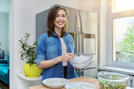 在冰箱附近的厨房里微笑的女人 用冰来冷却食物家庭桌子女士冷藏饮食沙拉蔬菜器具房子玻璃图片