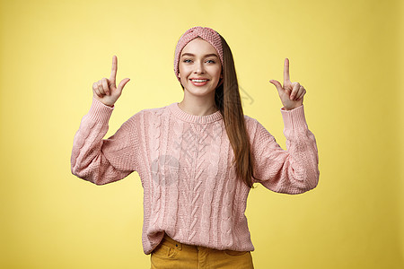 随和美丽的年轻女学生穿着针织毛衣 头带朝上 宣传广告 开心地微笑 心情愉快 在黄墙上对着镜头咧嘴笑女朋友快乐大学女孩培训班幸福购图片