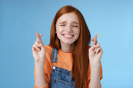 真诚充满希望的可爱红发女孩相信奇迹闭上眼睛忠实地祈祷交叉手指好运希望梦想成真让愿望渴望听到积极的结果 期待蓝色背景欲望喜悦微笑头图片