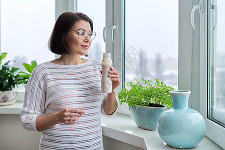 中年妇女在家里靠近窗户的地方喝牛奶饮料 瓶装液体酸奶饮食女性食物快乐微笑房子瓶子营养女士活力图片