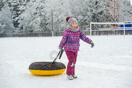 一个冬天的小女孩 穿着紫色衣服和一个充气圈 在一片雪覆盖的森林里走在街上新年童年微笑圣诞礼物手套骑术游戏帽子孩子们女孩图片