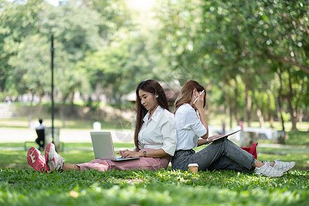 两个女孩在公园与笔记本电脑和数字平板电脑一起工作和学习 校对图片