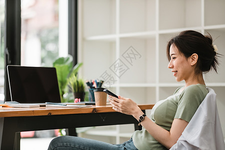 在现代办公室使用移动电话的快乐的亚洲女性妇女手机网络技术女士工作微笑商务人士屏幕社会图片