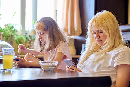 孩子们 两个女孩姐妹在家里吃东西 看智能手机的小孩娱乐生活现实青春期学生小吃孩子电话食物家庭图片