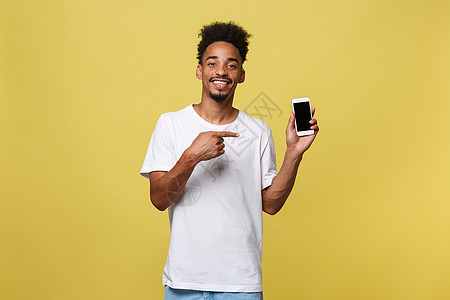 黄色背景中孤立的迷人年轻黑人肖像 手持空白智能手机 对着镜头微笑 竖起大拇指 感到快乐商务拇指细胞企业家男人男性展示衬衫电话商业图片
