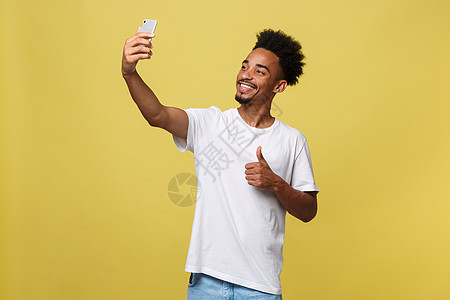 年轻的非裔美国黑人微笑着开心地用手机自拍自拍照片看起来很兴奋在通信技术的黄色背景中摆出酷炫的姿势乐趣爆炸快乐电话成功成人摄影细胞图片