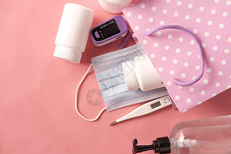 粉红色背景的外膜 温度计和手消毒剂液体桌子消毒剂预防外科安全医疗织物面具口罩图片