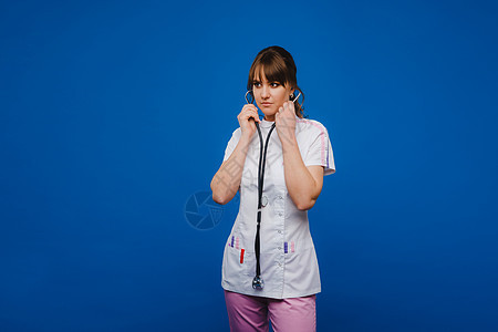 一位女医生在医院的医生办公室里打着手势 用蓝色背景中突显的听诊器检查心跳女孩保健诊所病人健康诊断工作从业者疾病护士图片