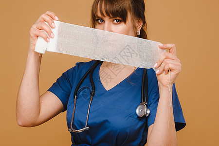 一名穿白外套的女医生在棕色背景上为伤口包扎伤口而持有扭曲的纱布绷带药店医院敷料帮助成人专家工作药品疾病女士图片
