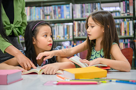 老师教学时 两个可爱的女孩在图书馆看书时发生冲突 人们的生活方式和教育 学校概念中的青年友谊和儿童关系 日托主题图片