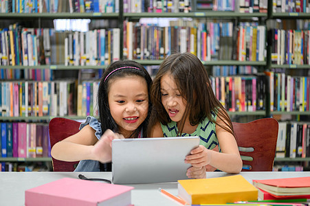 两个快乐可爱的小女孩在学校图书馆的平板电脑计算设备上玩耍 教育和自学无线技术概念 人们的生活方式和友谊 学龄前儿童学生图书馆学校图片