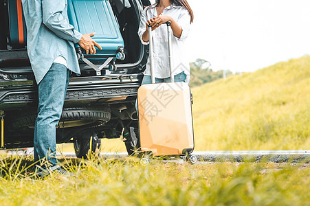 夫妇的特写下半身在 SUV 汽车后备箱后面沿着秋季山丘背景的公路旅行放下手推车行李 自由朋友之路 两人生活方式交通旅行图片