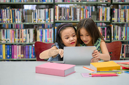两个快乐可爱的小女孩在学校图书馆的平板电脑计算设备上玩耍 教育和自学无线技术概念 人们的生活方式和友谊 学龄前儿童冲浪童年学校孩图片