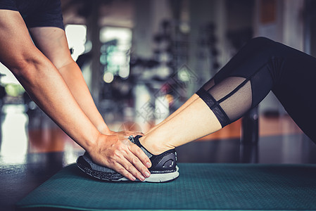 健身教练的手抓住健身女人的腿来训练紧缩扭曲锻炼 健康和保健 锻炼和力量主题图片