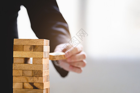 商务人士在堆叠塔上手工采摘一块木块作为启动项目 商业组织和公司成长进步 战略和金钱投资的成功 风险管理图片