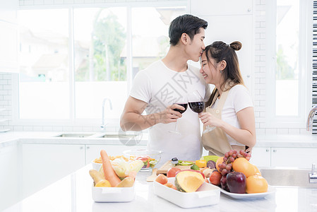 亚洲恋人在厨房里 男人亲吻女人的额头 同时互相碰杯 家庭和夫妻的概念 蜜月和假期主题图片