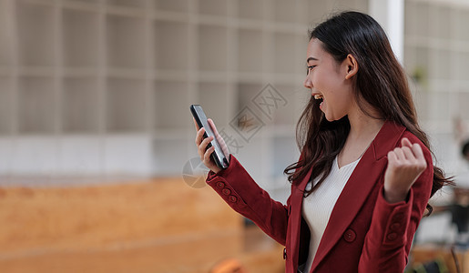 手握手机并兴奋成功任职的笑脸亚洲女性 一手一拳幸福喜悦胜利电话技术女孩优胜者商业成人快乐图片