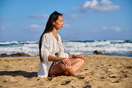 在沙滩上冥想时 处于莲花姿势的年轻美女假期海景海洋蓝色活力天空身体支撑沉思海滩图片