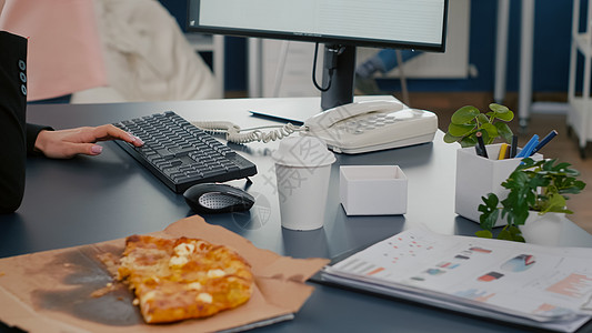 女商务人士在电脑前坐在桌子上吃披萨切片的密闭公司商务邮递员办公室公用经理职场电话图表生意人图片
