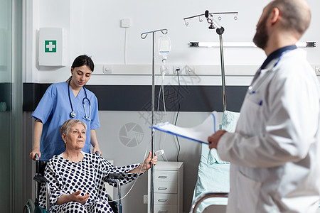 生病的老年老妇坐在轮椅上 手臂上有IV滴滴袋医师医生护士住院手术静脉外科女士临床保健图片