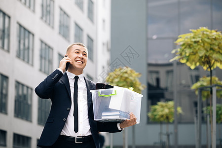 快乐的人用盒子里的东西通电话 手机通话 讲电话 办公楼之间的一名员工拿着一个盒子 文件上有一朵桌花图片