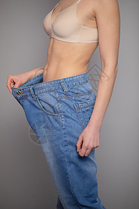 女人显示她减肥和穿着她的旧牛仔裤 穿着宽大牛仔裤的苗条女孩展示了她在开始吃健康食品后是如何减肥的卧室数字饮食测量损失腰部节食裤子图片