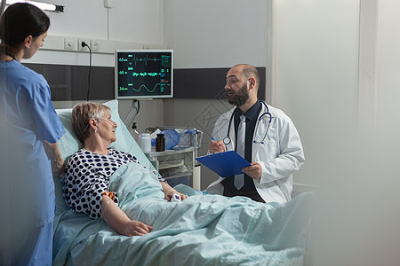 医生与坐在床边的老年病人交谈医院关爱外科讨论药品手术笔记会议输液袋从业者图片
