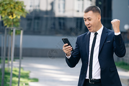 在智能手机户外阅读好消息的兴奋人的画像 成功的商务人士在外面用手机庆祝胜利 惊讶的男人在外面看手机街道应聘技术应用快乐商务短信电图片