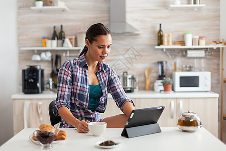 妇女在平板电脑上读新闻芳香绿茶工具主妇茶杯手指女士技术早餐桌子图片
