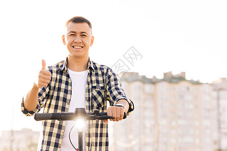 白种人嬉皮士靠在电动滑板车上看着相机 竖起大拇指 时髦的人在户外的车辆上 生态友好的现代城市交通 生态与城市生活方式图片