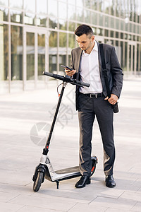 一名男性商务人士接近电动滑板车并使用手机应用程序 生态交通 男子在城市中使用电动滑板车作为现代交通工具图片