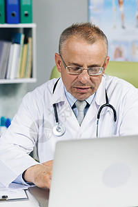 戴眼镜的冷静家庭医生正在健康诊所的笔记本电脑上工作 穿白色实验室大衣的医生正在医院办公室的桌子后面浏览病史图片