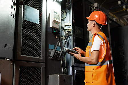 一名身穿安全帽和背心的电站工程师走到机架前 使用数字平板电脑检查电气控制室的电力系统 工业 工厂 能源的概念图片