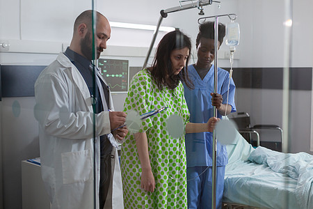 帮助有病的妇女从床上站起来 拿着静脉注射液滴水袋的静脉注射图片