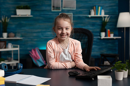 坐在家庭办公桌旁的小小学孩子的肖像视频女学生笔记本学习互联网技术导师演讲教育微笑图片