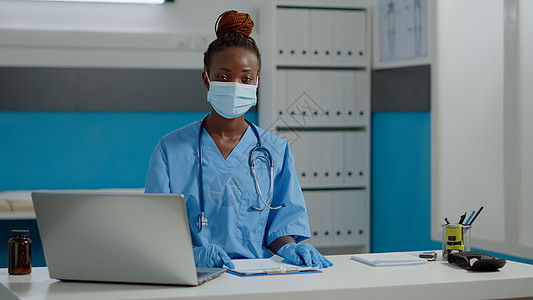 护士用笔记本电脑和文件坐在书桌的护士肖像职业内阁医院诊断大衣卫生咨询手套女士疾病图片