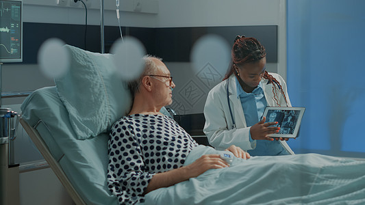 在平板上向病人解释X光的非洲美籍医生监视器药品医院技术帮助监护卫生单元设施长老图片