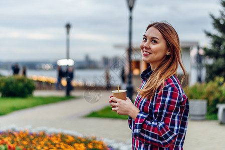 美丽的年轻女子拿着咖啡杯 在公园笑着微笑喜悦衬衫女性头发日落杯子快乐女孩金发女郎女士图片