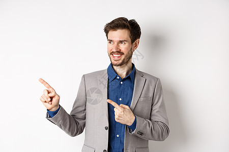 身穿灰色西装的成功商务人士手指向左 看着横幅 自信地微笑 展示广告 站在白色背景下成人人士工作男性推销员企业家胡子商务套装情绪图片